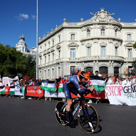 Un ciclista del equipo Jayco AlUla pasa junto a personas con banderas y pancartas en apoyo a los palestinos en Gaza, en la última etapa de la Vuelta a España, en la madrileña Plaza de Cibeles