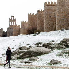 Una mujer camina junto al lienzo norte de la muralla de Ávila cubierta por una fina capa nieve caída en las últimas horas. EFE