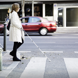 Una persona con discapacidad visual cruzando un paso de peatones ayudándose con un bastón. / ONCE