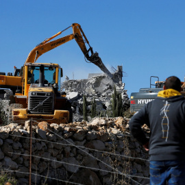 19/11/2019. - Dos hombres observan cómo maquinaria israelí demuele una casa palestina cerca de Hebrón. / REUTERS