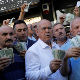 Varias personas sostiene billetes de dólar delante de una oficina de cambio em Ankara, respondiendo a la llamada del presidente Erdogan a cambiar billetes verdes par sostener la lira turca. REUTERS/Umit Bektas