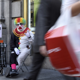 Rayito, un mendigo disfrazado de payaso, saluda sentado junto a un cartel que dice "Quiero comer, gracias" en la calle Gran Vía, en el centro de Madrid, el 28 de octubre de 2014.