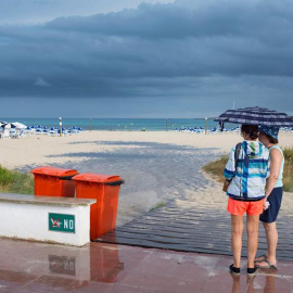 Dos mujeres se resguardan de la lluvia bajo un paraguas en la playa de Punta Prima, en el municipio de Sant Lluís (Menorca), en una jornada en la que la Agencia Estatal de Meteorología (Aemet) ha activado la alerta amarilla en Baleares por posibles prec