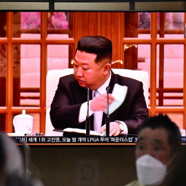 La gente se sienta cerca de una pantalla que muestra una transmisión de noticias en una estación de tren en Seúl el 12 de mayo de 2022, del líder de Corea del Norte, Kim Jong Un, quitándose una máscara facial en la televisión para ordenar cierres e