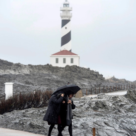 Dos personas caminan por las inmediaciones del faro de Faváritx, en el municipio de Mahón, en una jornada en la que la borrasca Gloria, que trae este domingo un temporal de lluvia, nieve, viento y olas, ha puesto en alerta roja a la Comunidad Valenciana