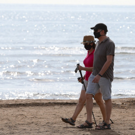 Dos personas protegidas con mascarilla pasean por la playa de la Malvarrosa durante su franja horaria permitida en la desescalada ante la crisis del Covid-19 en la que mayores de 14 años y menores de 69 tienen permitidas las salidas para pasear y hacer d