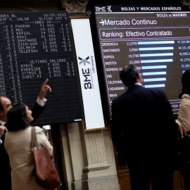 Cuatro personas frente a un panel de valores del Ibex 25 en el Palacio de la Bolsa, a 30 de mayo de 2022, en Madrid.