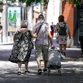 Una pareja de ancianos camina por la calle con un carro de compra.