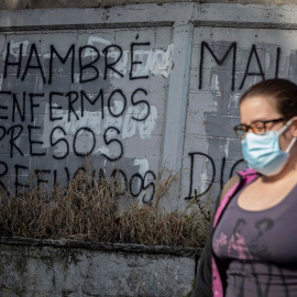 Una mujer camina frente a una pared con un graffiti pintado que dice "Hambre, enfermos, presos, refugiados" el 8 de febrero de 2021, en Caracas (Venezuela).