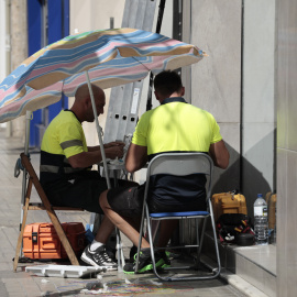 Dos operarios de telefonía se protegen con una sombrilla del intenso sol y calor en Valencia.