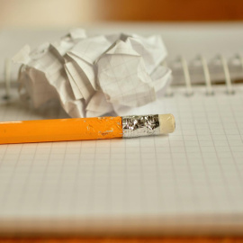 Un cuaderno con una hoja arrugada encima y un lápiz.