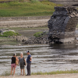 Tres personas junto al río Miño, cuyo bajo caudal ha dejado a la vista las ruinas del antiguo Portomarín, que en los años 60 del siglo pasado fue anegado por el embalse de Belesar