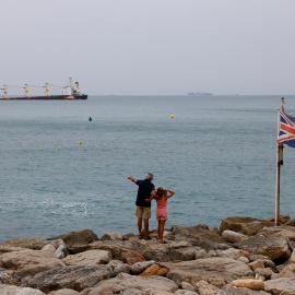 Un hombre y una niña observan desde la orilla, junto a una bandera británica, al granelero OS35, medio hundido frente a Gibraltar. REUTERS/Jon Nazca