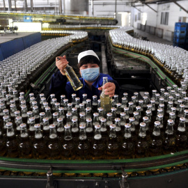 Una mujer recoge botellas de cerveza en una cadena de montaje dentro de una fábrica en Shenyang. REUTERS