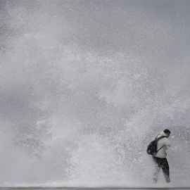 Un ciudadano desafía el fuerte oleaje en la playa de Barceloneta, durante el temporal marítimo que afecta a toda la costa catalana. EFE/ Andreu Dalmau