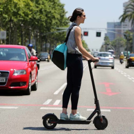 Una joven cruza un paso de peatones con un patinete eléctrico.