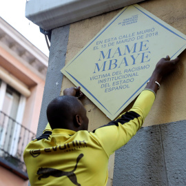 15/03/2019.- Un hombre coloca un placa durante la concentración convocada por el Sindicato de Manteros esta tarde en la plaza de Nelson Mandela, en Madrid, en recuerdo a Mame Mbaye, cuando se cumple un año de la muerte por un infarto de este vendedor se