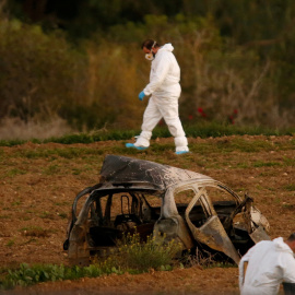 Expertos forenses caminan en un campo después de que una bomba explotara un automóvil (primer plano) y matara a la periodista de investigación Daphne Caruana Galizia en Bidnija, Malta, el 16 de octubre de 2017