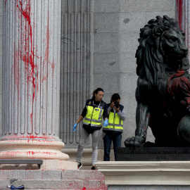 Efectivos de la Policía Nacional inspeccionan uno de los leones del Congreso, cubierto con pintura roja tras la acción reivindicativa de un grupo de activistas