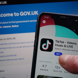 Un usuario se descarga TikTok en su teléfono móvil mientras consulta la página web del Gobierno de Reino Unido.