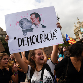 Una mujer sostiene un cartel que muestra al presidente de Gobierno, Mariano Rajoy, y al dictador Francisco Franco, sobre el mensaje "Democracia", durante la manifestación en repulsa de las escenas de violencia policial que se vivieron el 1-