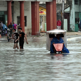 Varias personas caminan por una calle llena de agua, hoy en La Habana