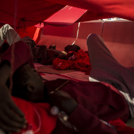 Dos migrantes se protegen del sol bajo una manta en el puerto del Algeciras. Han pasado varias noches allí debido al colapso en los polideportivos y dependencias policiales tras llegar en patera a España. JAIRO VARGAS