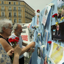 (22/5/22) Varias personas colocan claveles en un mural con retratos de colaboradores en la búsqueda de víctimas por el robo de bebés en España, a 22 de mayo de 2022.