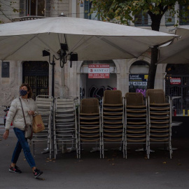 Una mujer pasa junto a la terraza recogida de un bar cerrado.