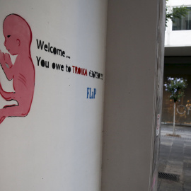 Una pintada en una calle de Atenas de un dibujo de un recién nacido con una frase que dice:  "Bienvenido ... le debes a la Troika 36.730 €". REUTERS / Alkis Konstantinidis