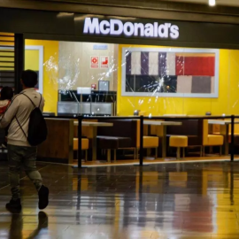 Dues persones passen davant de l'aparador del McDonald's amb els vidres trencats al centre comercial Màgic Badalona