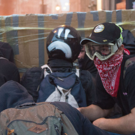 Varios jóvenes encapuchados se protegen de las balas de goma con un parapeto de cartón y cinta de embalaje, durante los disturbios de Barcelona. GUILLEM SANS