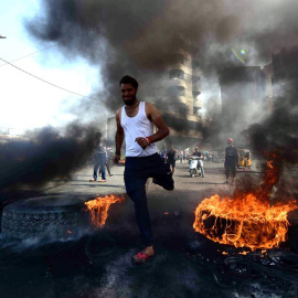 Un manifestante corre entre rueda de coche ardiendo durante una manifestación en la plaza de Khillani en Bagdad, Irak.EFE/ Murtaja Lateef