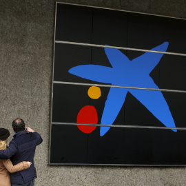 Una pareja se hace un selfie junto a una de las oficinas de Caixabank en Madrid. REUTERS