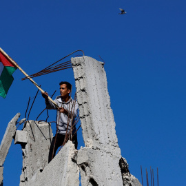 Un hombre sostiene una bandera palestina sobre las ruidas de una de las casas destruidas por los bombardeos de Israel en la Franja de Gaza. REUTERS/Mohammed Salem