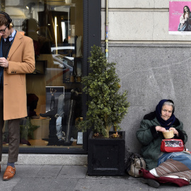 Un hombre consulta a su móvil junto a una tienda en cuya puerta hay una mujer pidiendo limosna, en el madrileño barrio de Salamanca. AFP/Gerard Julien