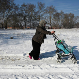 Una mujer empuja por la nieve el carro con su hijo en un campo de refugiados en Grecia. REUTERS