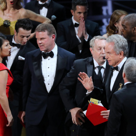 Los socios PricewaterhouseCoopers (PwC), Martha Ruiz y Brian Cullinan (a la izquierda de la imagen), conversan en el escenario de la gala de los Premios Oscar de Hollywood, mientras un regidor conversa con el actor Warren Beatty, quien sost