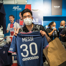 Un aficionado hace el signo de la victoria mientras sostiene la camiseta con el nombre y el número de Lionel Messi en el Paris Saint Germain, en la tienda oficial del equipo en los Campos Elíseos de París. EFE/CHRISTOPHE PETIT TESSON