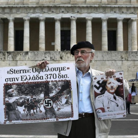 Un hombre sostiene un cartel de la canciller Angela Merkel como si fuera un miembro del partido nazi frente al Parlamento griego en la marcha por el Día de los Trabajadores en Atenas. /EFE