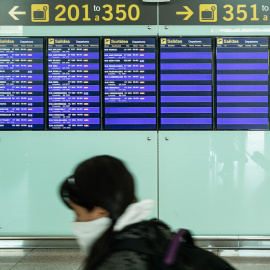 Una pasajera con mascarilla observa los paneles del aeropuerto El Prat de Barcelona, a 20 de marzo de 2020.