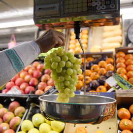 Un dependiente pesa un racimo de uvas en un mercado, a 31 de diciembre de 2023, en Madrid.