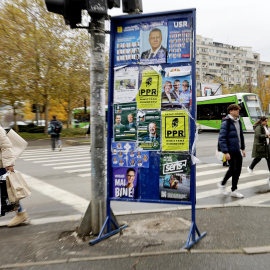 Una mujer pasa junto a un póster lleno de carteles electorales para las elecciones parlamentarias en Bucarest, Rumania.