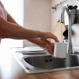 Una mujer llenando un vaso de agua en la pila de la cocina.