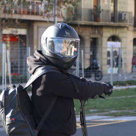 Una persona amb casc circulant per Barcelona amb un patinet