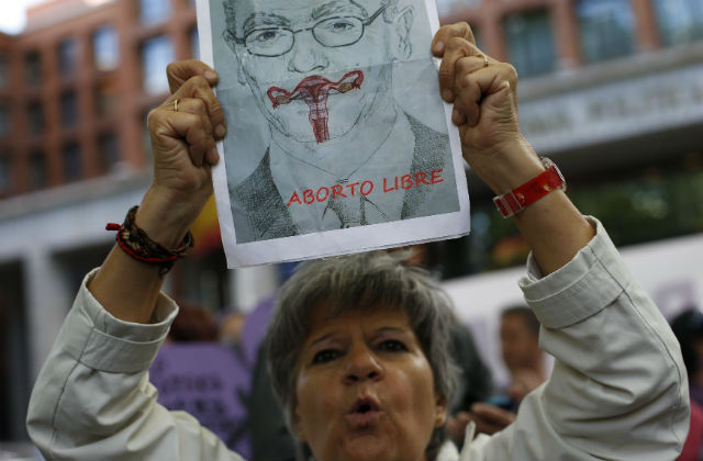 Una mujer levanta un cartel en el que un órgano reproductor femenino tapa la boca de Gallardón. REUTERS
