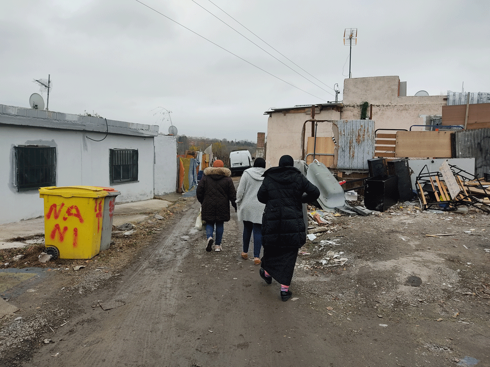 Las tres mujeres caminan hacia sus casas en una calle sin asfaltar y repleta de charcos y barro.